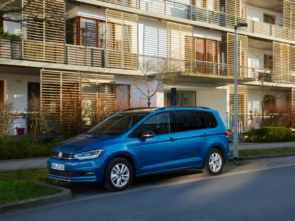 Volkswagen Touran kék színben, lakóház előtt